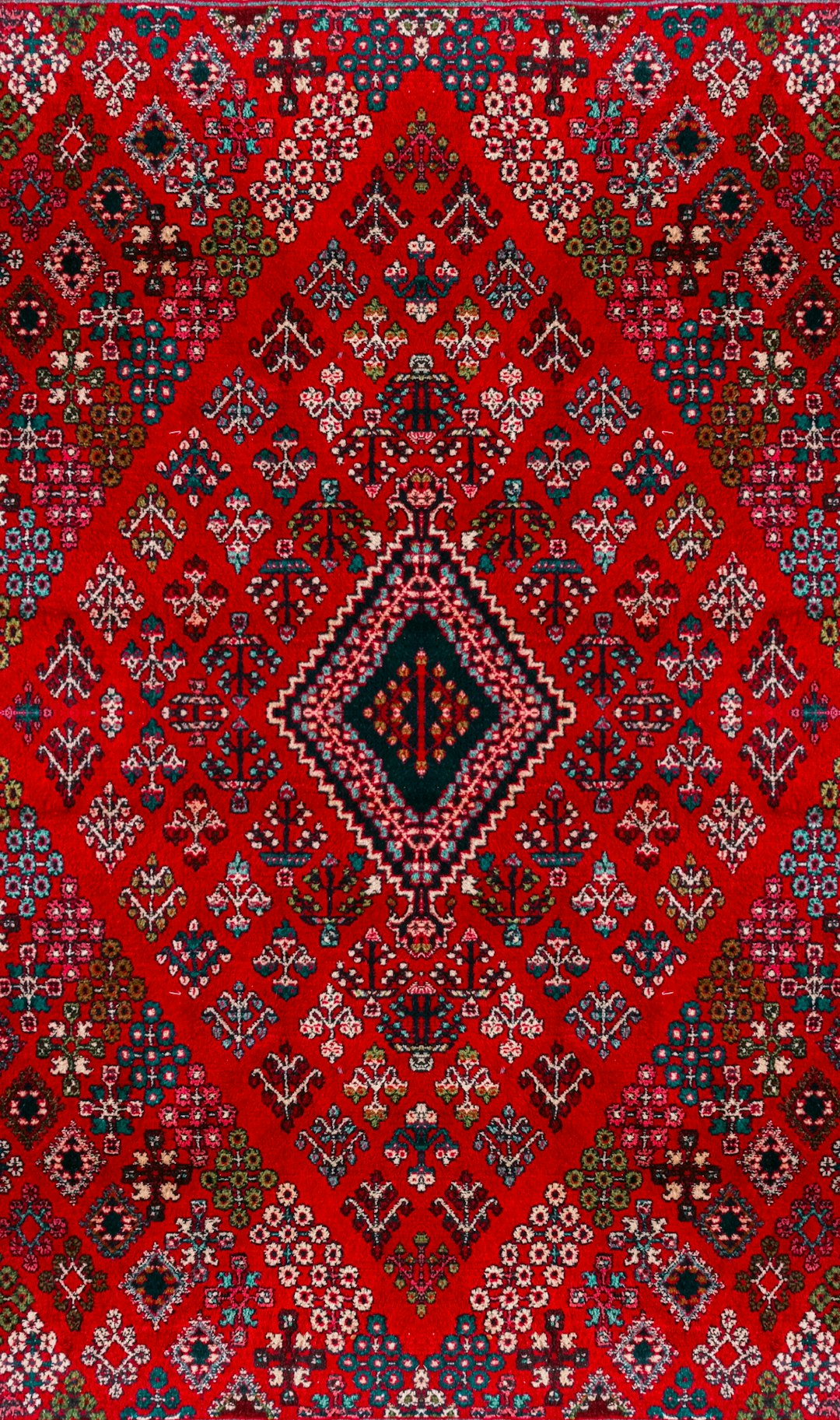 A red Persian rug with intricate geometric patterns and a central diamond motif